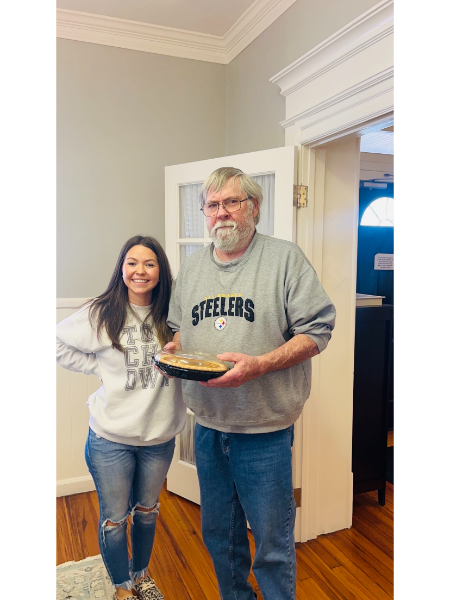 A man wearing a steelers sweatshirt stands next to a woman holding a pie.