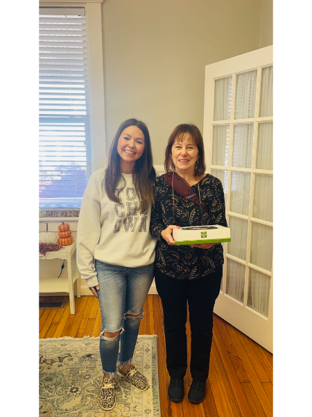 Two women are standing next to each other in a living room holding a box.