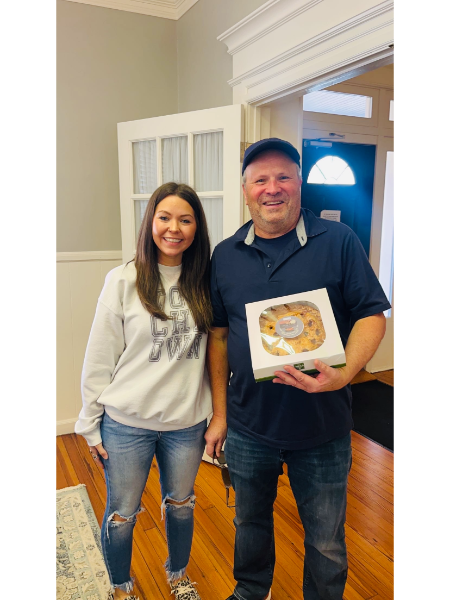 A man and a woman are standing next to each other holding a box of cookies.