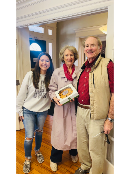 A man and two women are standing next to each other holding a box of food.