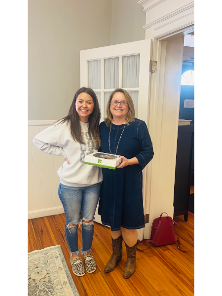 Two women are standing next to each other in a room holding a box.