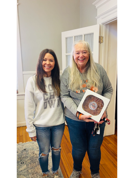 Two women are standing next to each other holding a box of chocolate cake.