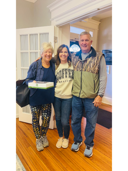 A woman wearing a coffee sweatshirt stands between two men