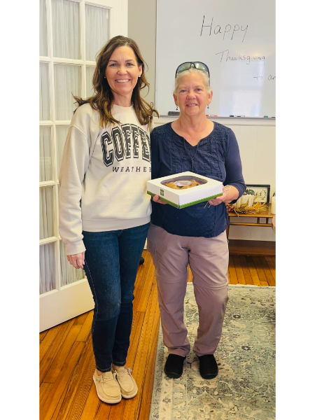 Two women are standing next to each other holding a box of food.