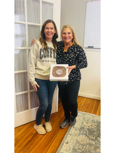 Two women standing next to each other holding a box of donuts