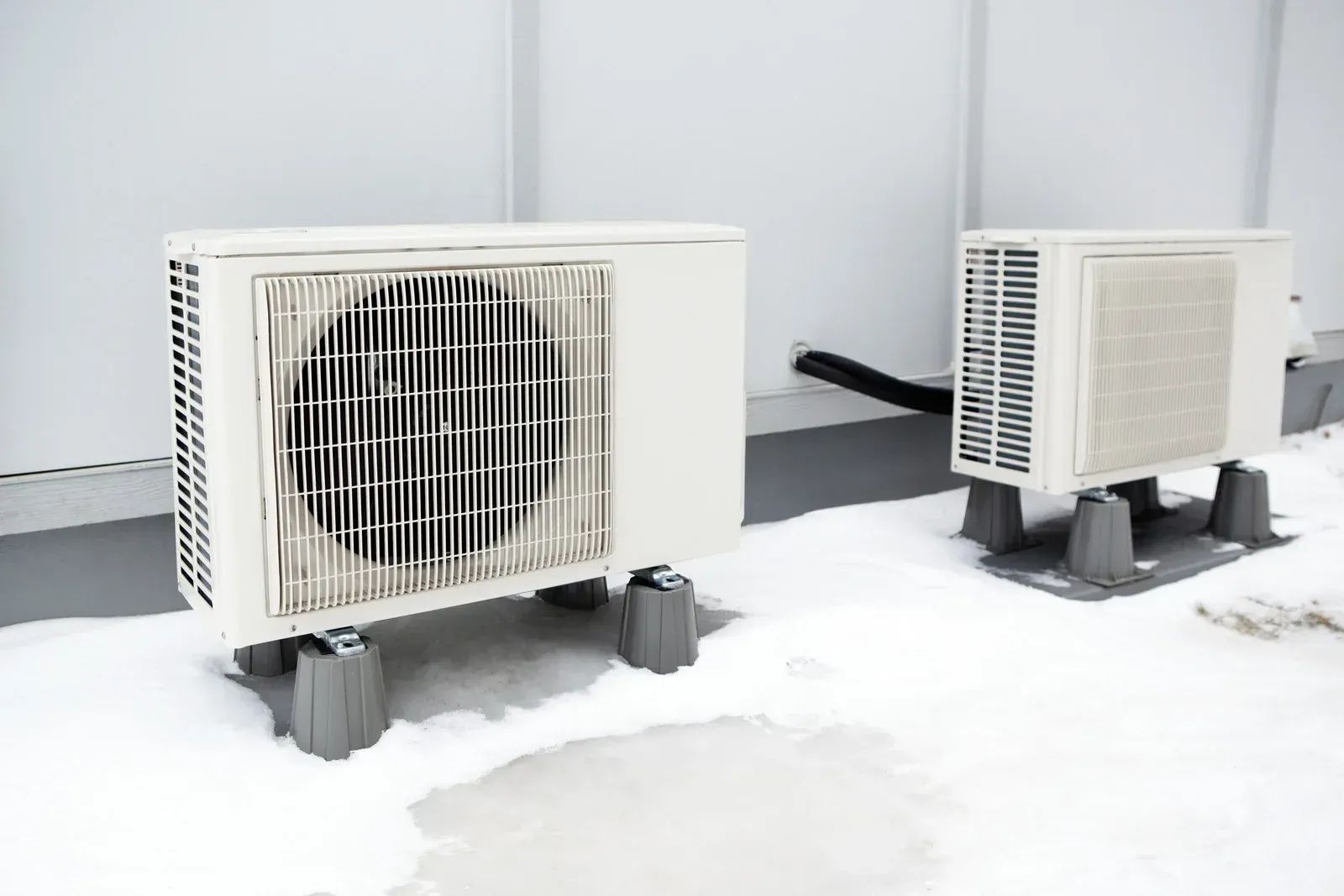 Two white outdoor air conditioning units on brackets in snow