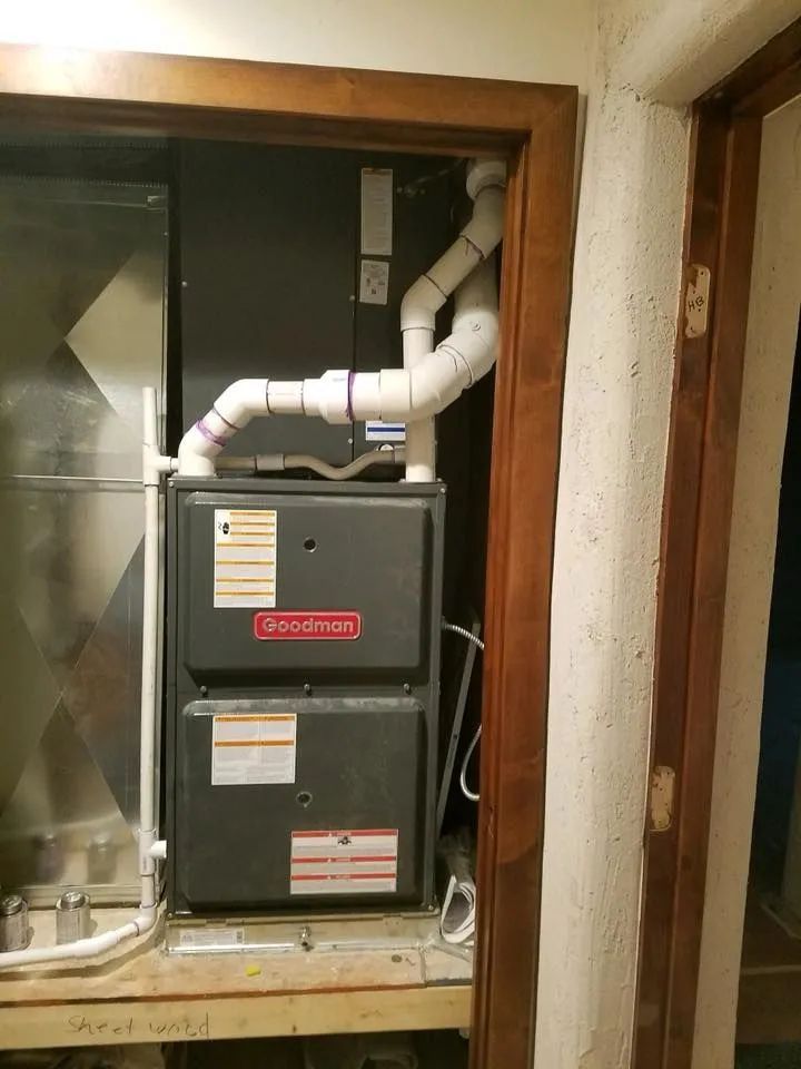A Goodman gas furnace with white PVC venting pipes installed in a wooden-framed utility closet.