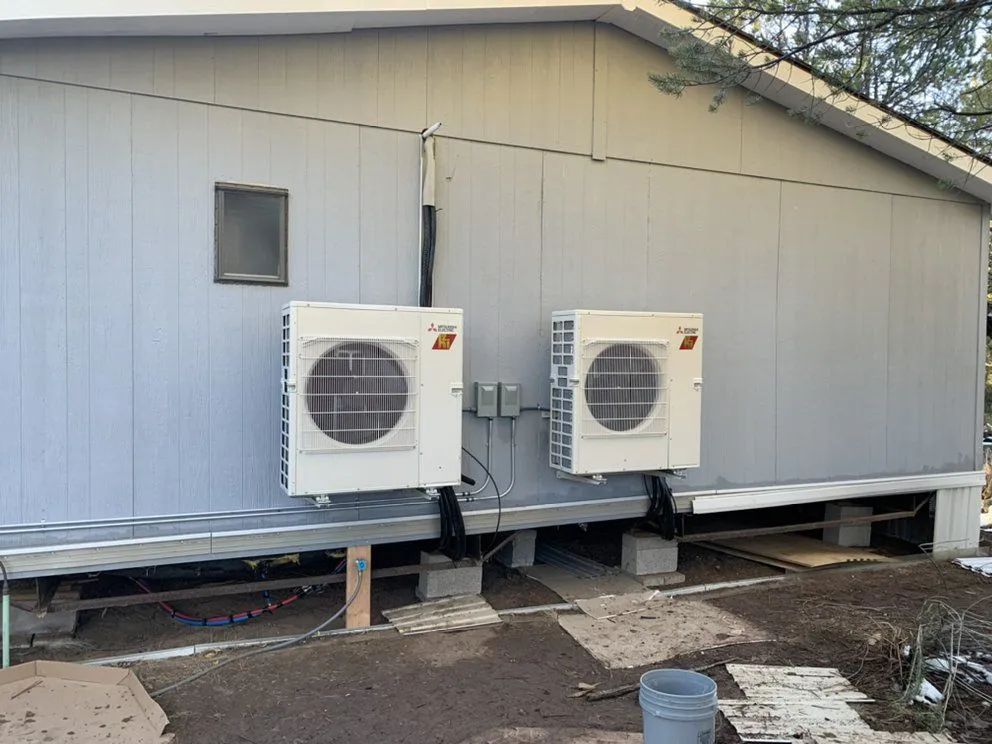 Two outdoor air conditioner units mounted on the side of a light gray building.
