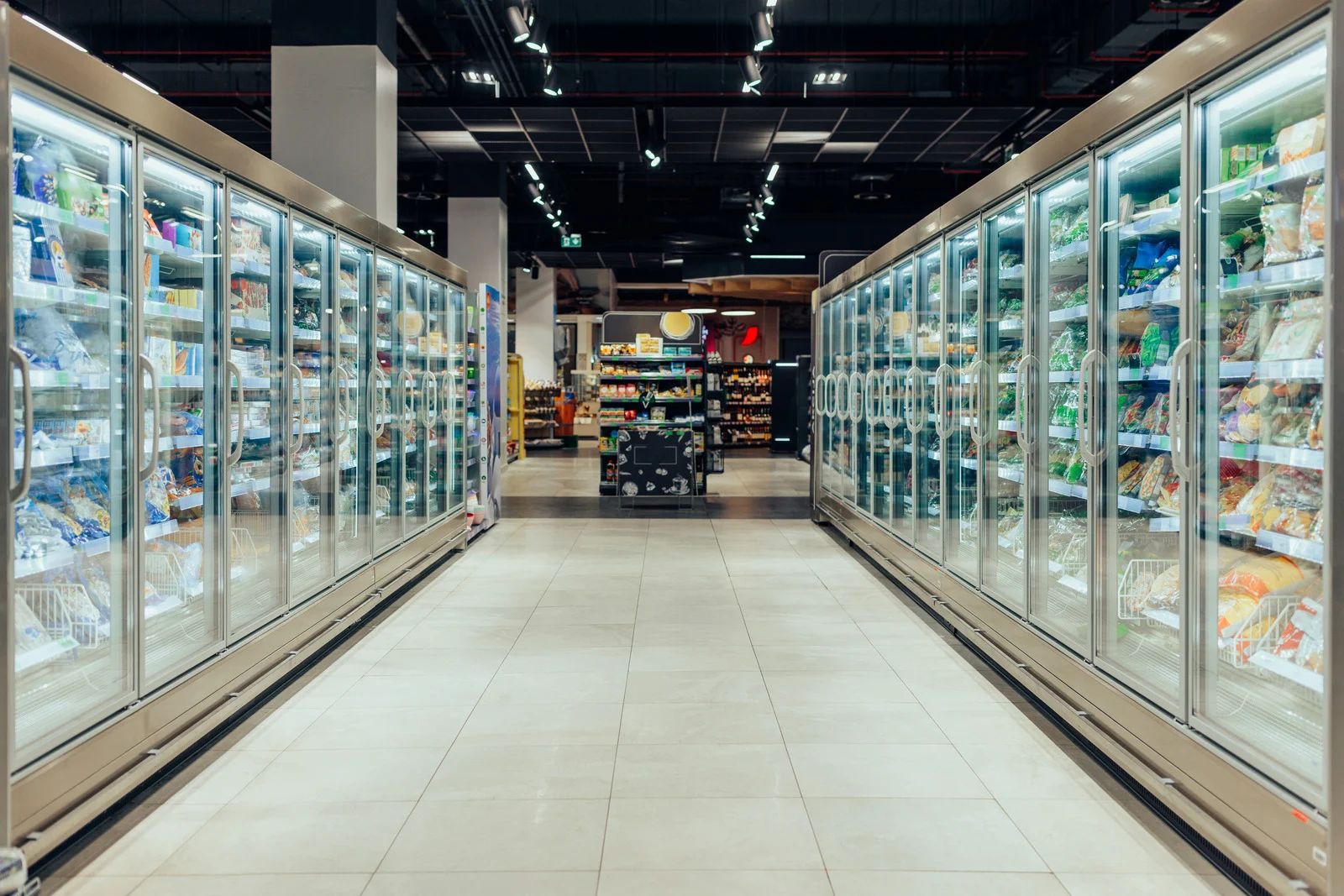 A grocery store aisle with rows of refrigerated display cases, filled with products.