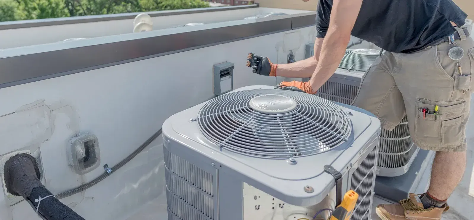 A man is working on an air conditioner on the roof of a building.