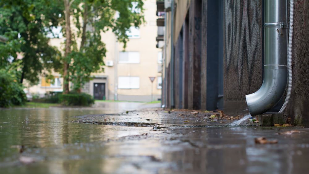 A Drainpipe Is Draining Water on A Flooded Sidewalk — Blair Merlehan Plumbing in Wagga Wagga, NSW