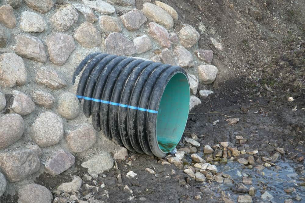 A Black Pipe with A Green Stripe on It Is Sitting in The Dirt — Blair Merlehan Plumbing in Wagga Wagga, NSW