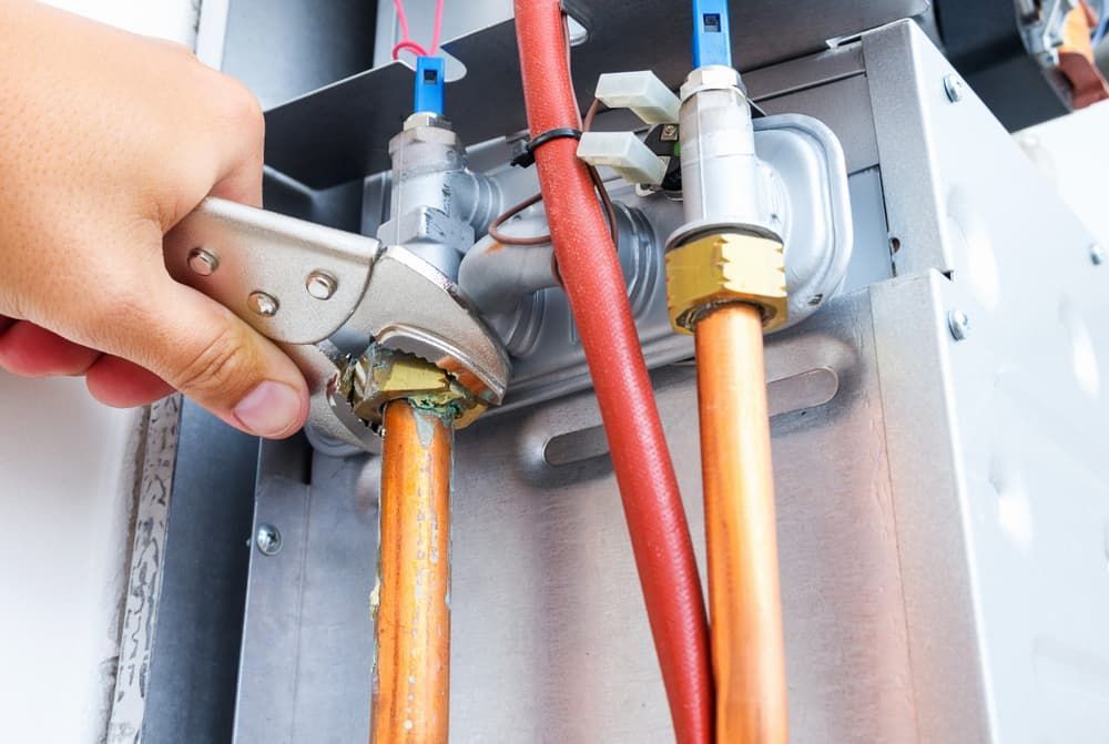 A Person Is Working on A Water Heater with A Wrench — Blair Merlehan Plumbing in Wagga Wagga, NSW