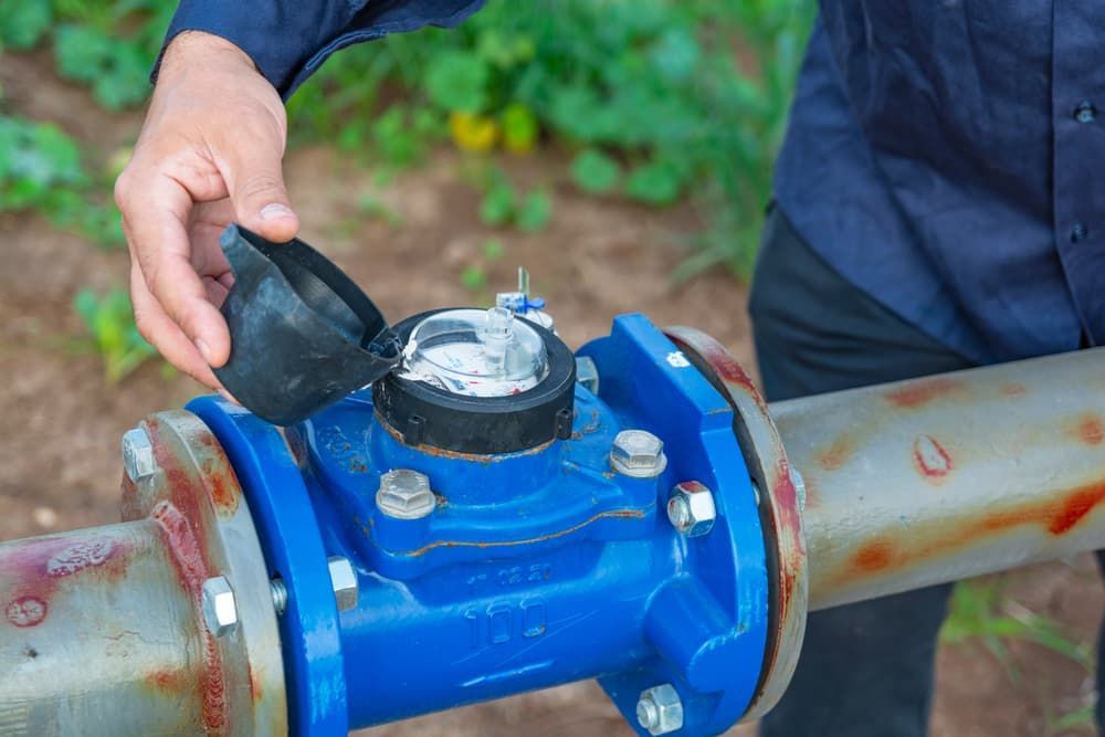A Man Is Fixing a Water Meter on A Pipe — Blair Merlehan Plumbing in Wagga Wagga, NSW