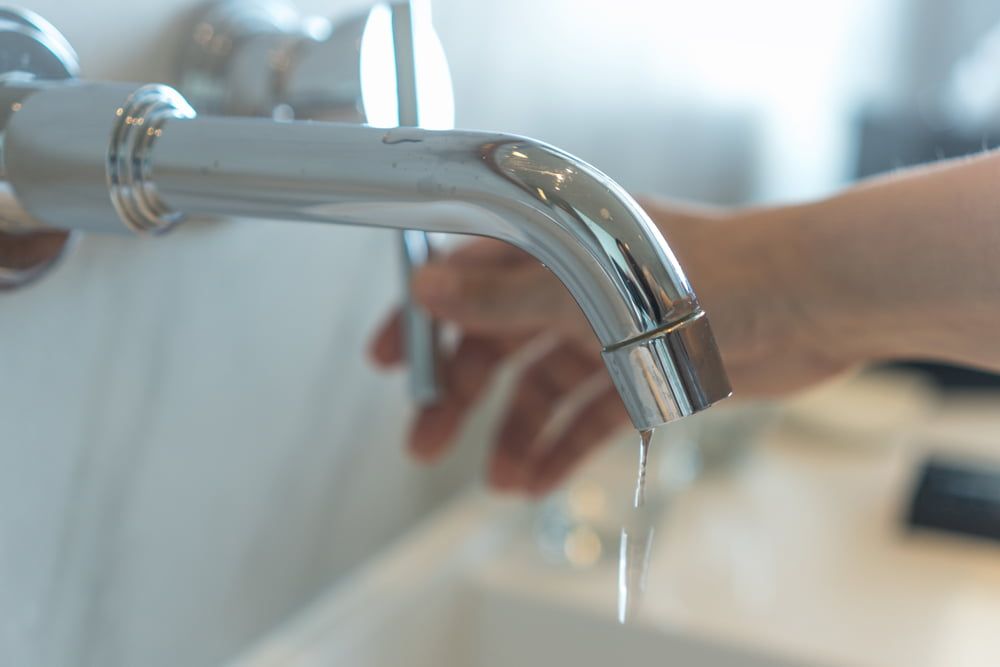 A Person Is Washing Their Hands Under a Faucet in A Bathroom — Blair Merlehan Plumbing in Wagga Wagga, NSW