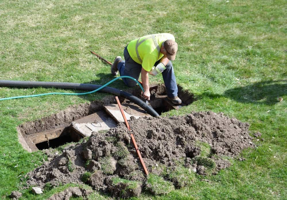 A Man Is Kneeling Down in The Dirt Next to A Hose — Blair Merlehan Plumbing in Wagga Wagga, NSW