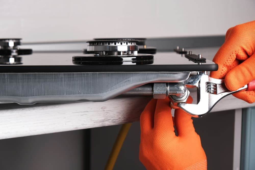 A Person Is Fixing a Gas Stove with A Wrench — Blair Merlehan Plumbing in Wagga Wagga, NSW