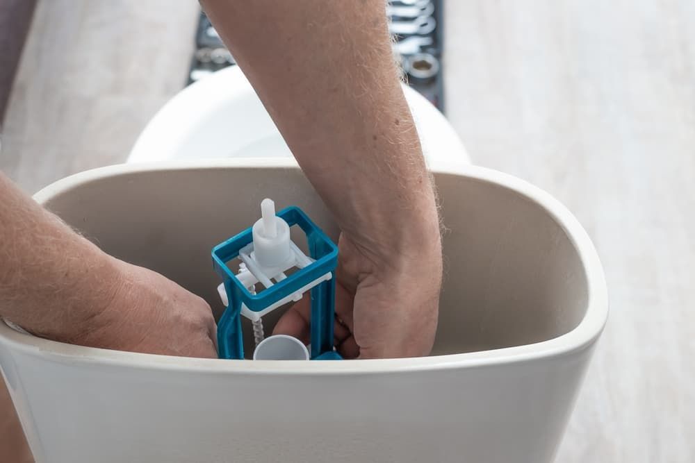 A Person Is Fixing a Toilet in A Bathroom — Blair Merlehan Plumbing in Wagga Wagga, NSW