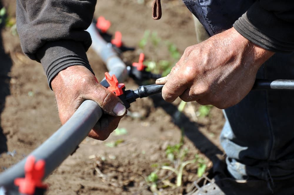 A Man Is Working on A Hose in The Dirt — Blair Merlehan Plumbing in Wagga Wagga, NSW