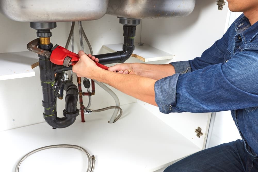 A Man Is Fixing a Sink with A Wrench — Blair Merlehan Plumbing in Wagga Wagga, NSW