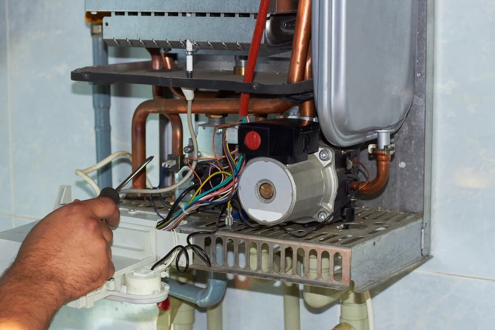 A Man Is Fixing a Boiler with A Wrench — Blair Merlehan Plumbing in Wagga Wagga, NSW