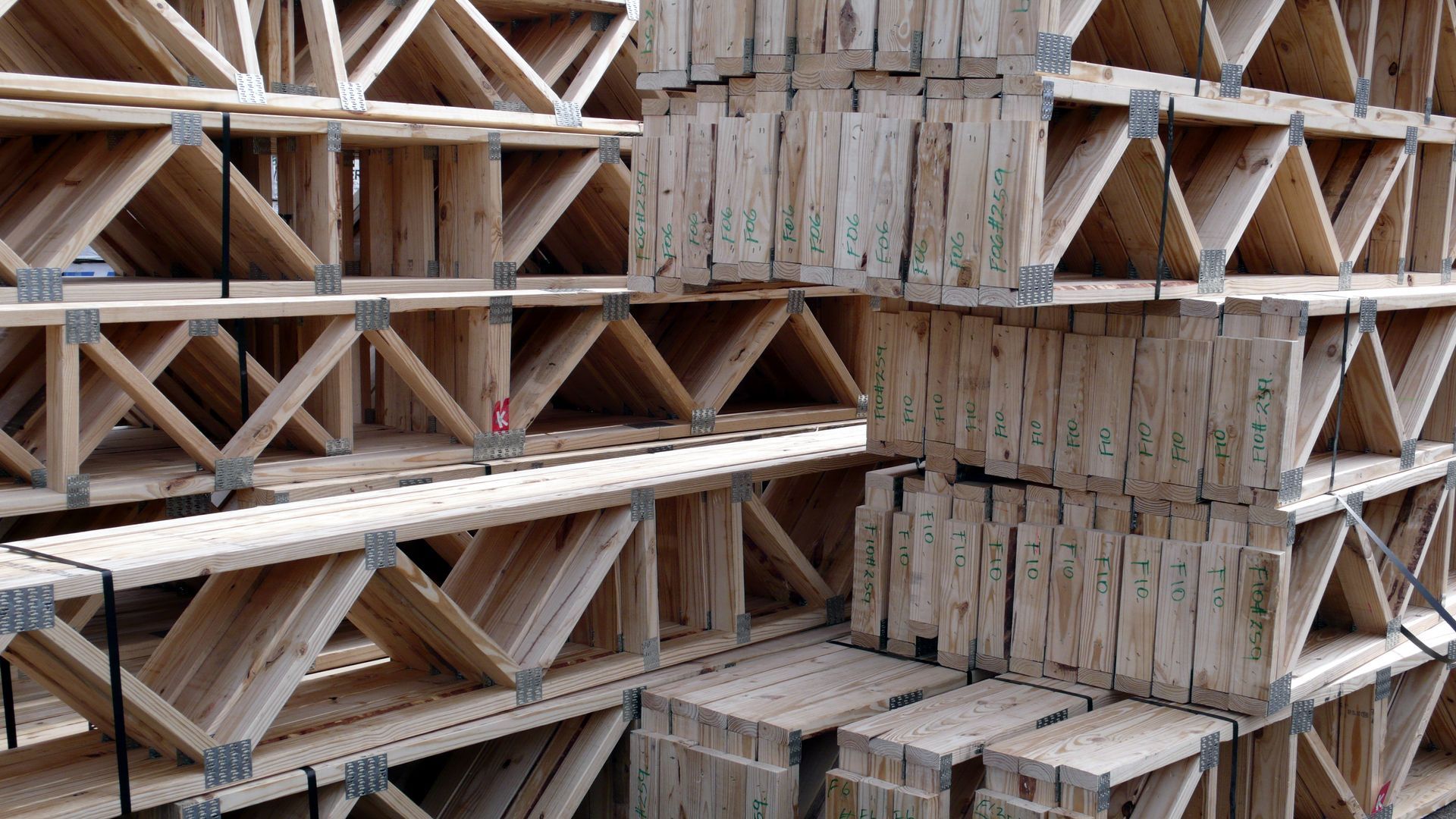 Stacks of wooden floor trusses arranged in rows at a construction supply site.