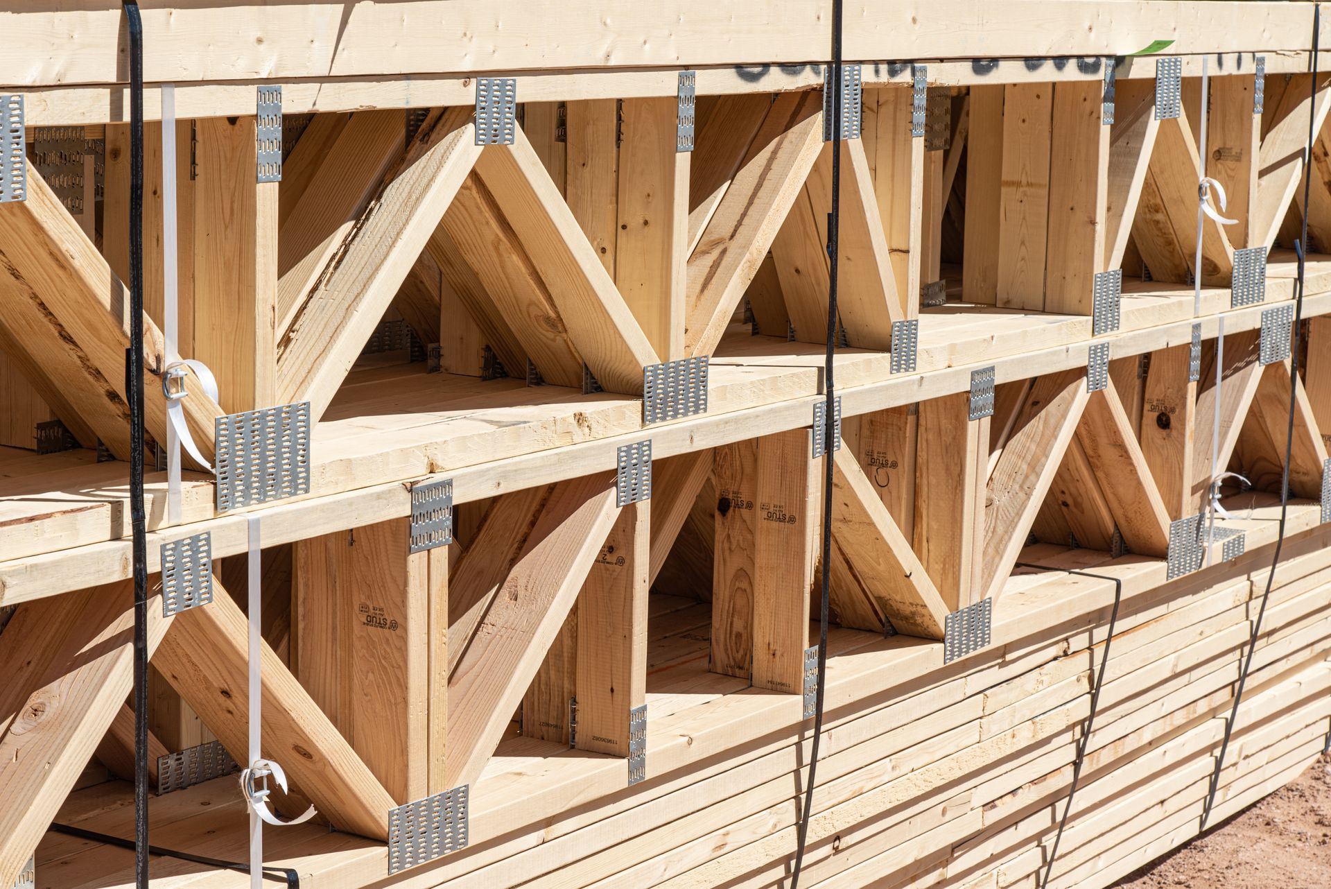 Stacked wooden floor trusses secured with metal plates at a construction site.