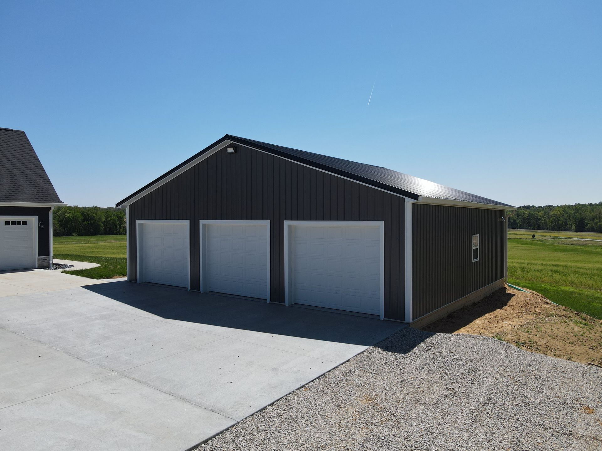 Dark gray garage with three white doors beside a concrete driveway under a clear blue sky