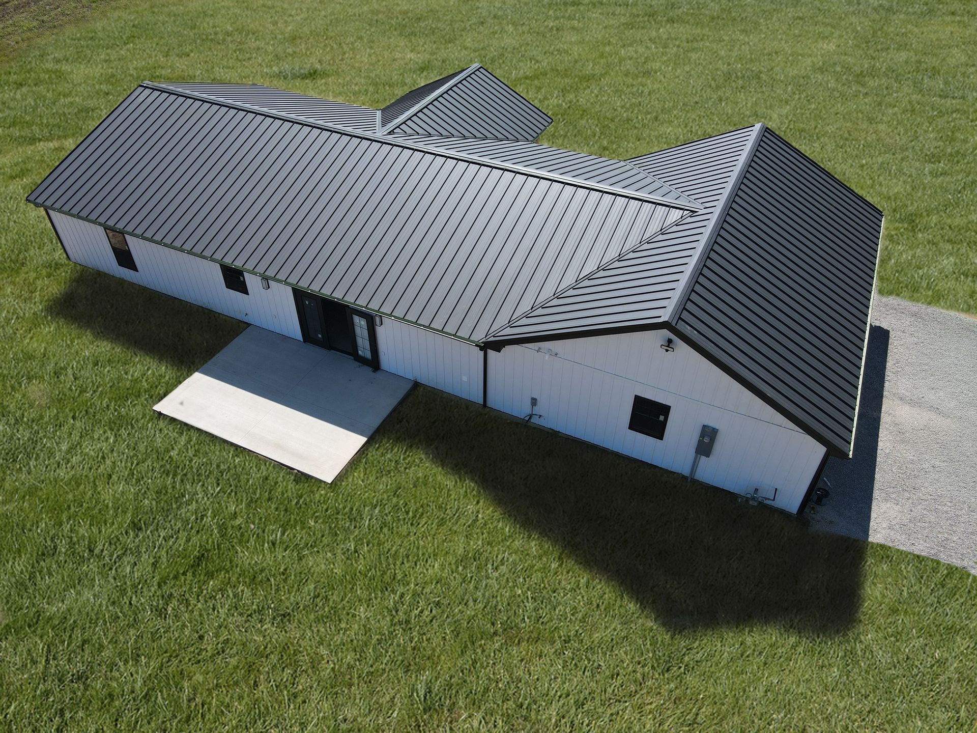 Aerial view of a white building with a gray metal roof on a grassy lot.