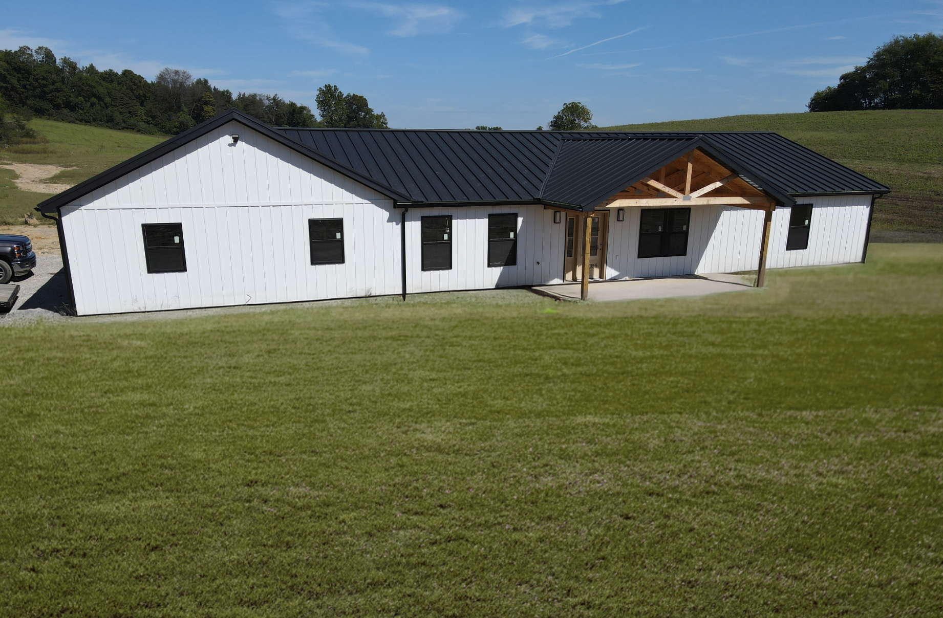 White single-story house with black roof and covered porch, set behind a large green lawn under a blue sky