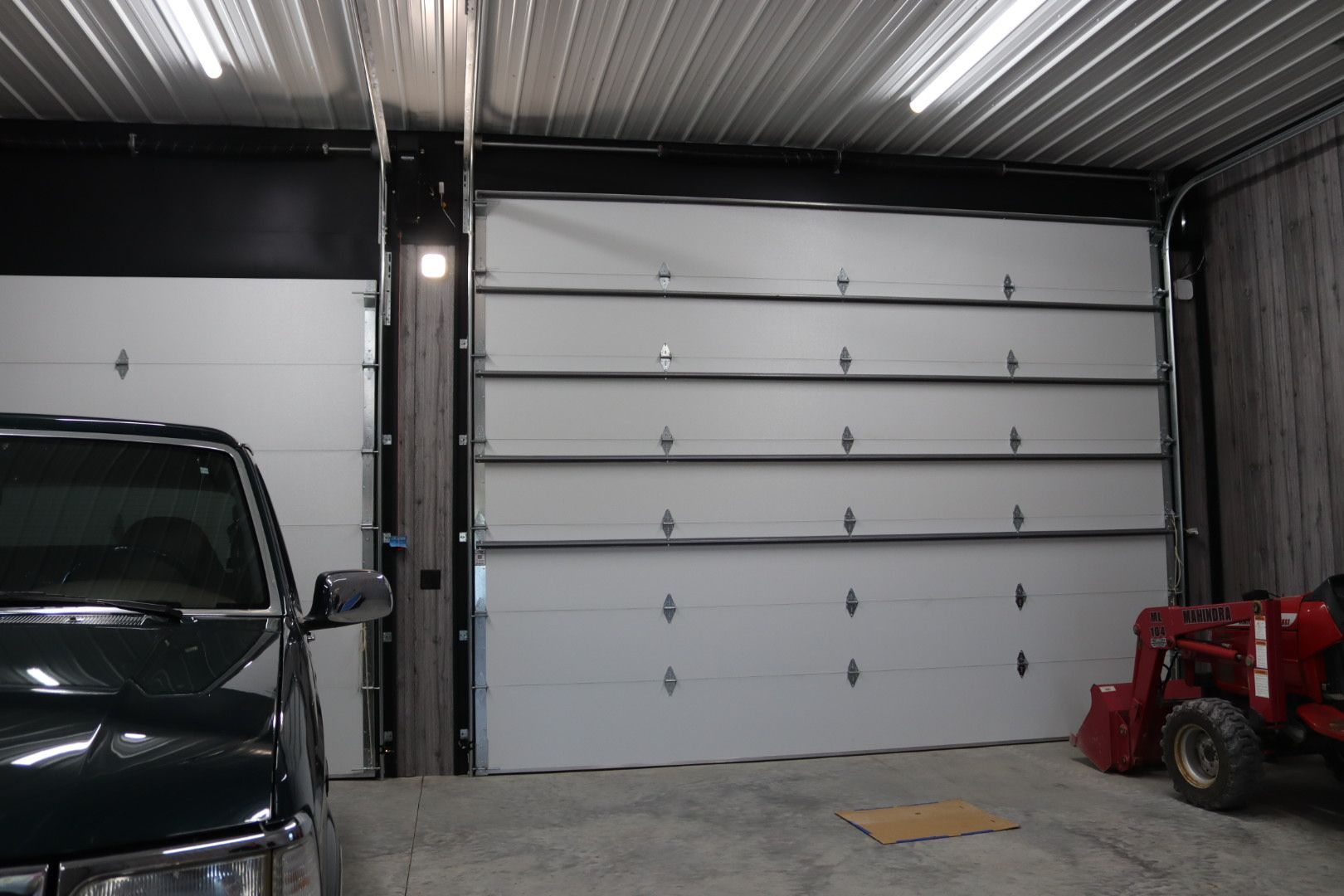 Garage interior with white sectional door, black SUV on left, and red tractor on right.