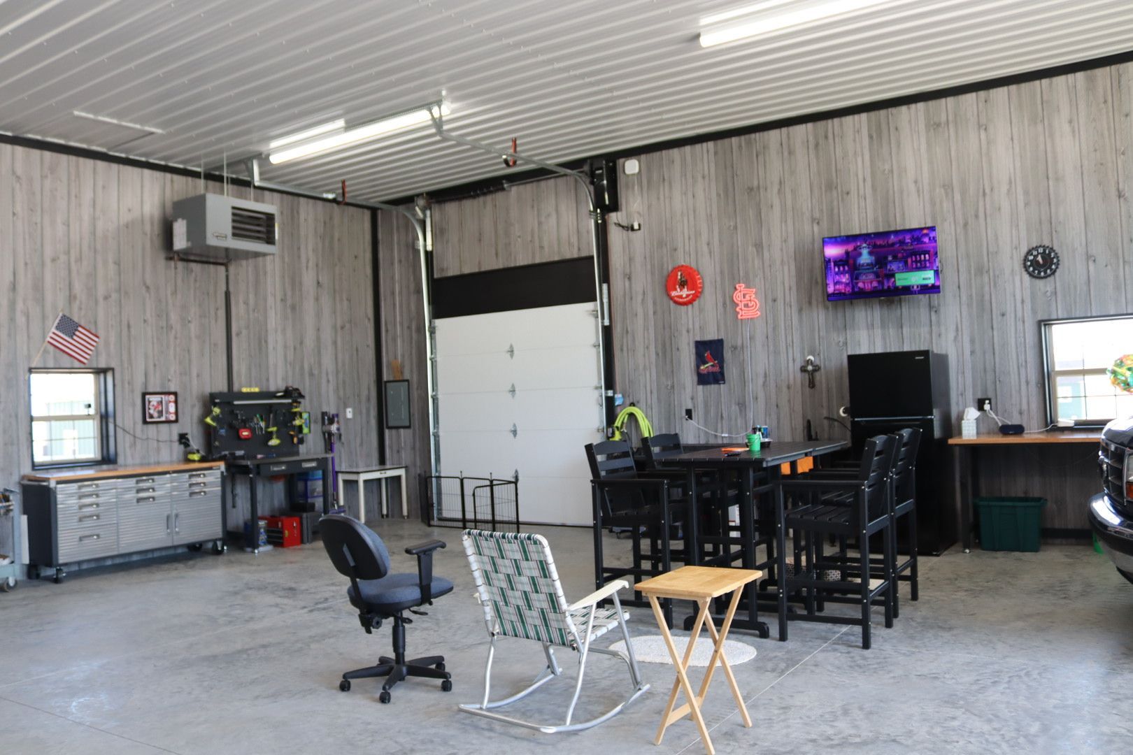 Industrial garage workspace with workbench, TV, chairs, and tools under a high metal ceiling