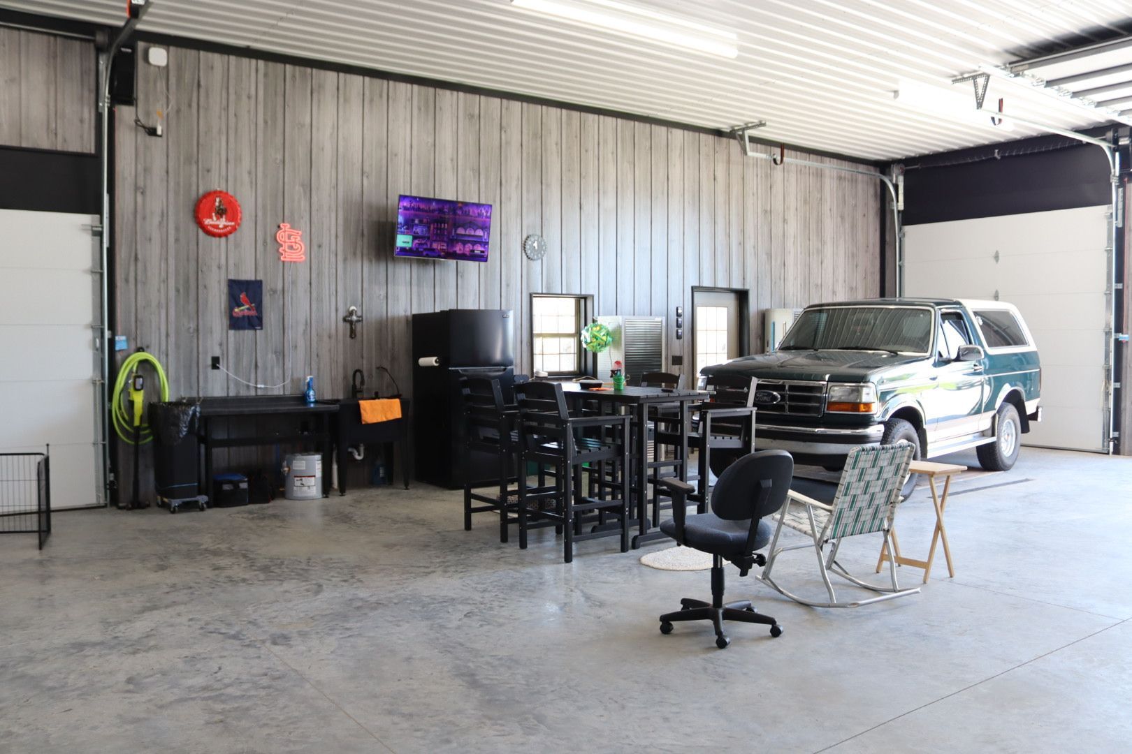 Workshop garage with a TV, chairs, desks, and an SUV parked inside