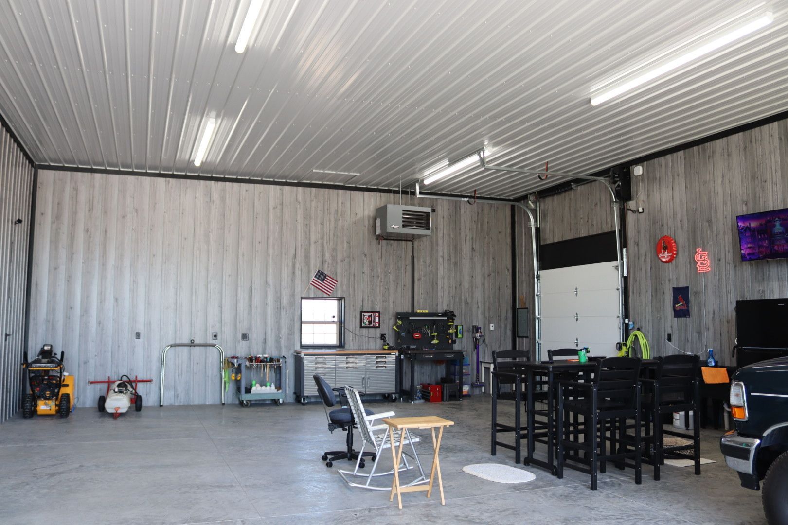 Spacious metal garage with storage, tools, workbench, and a dining table under bright ceiling lights