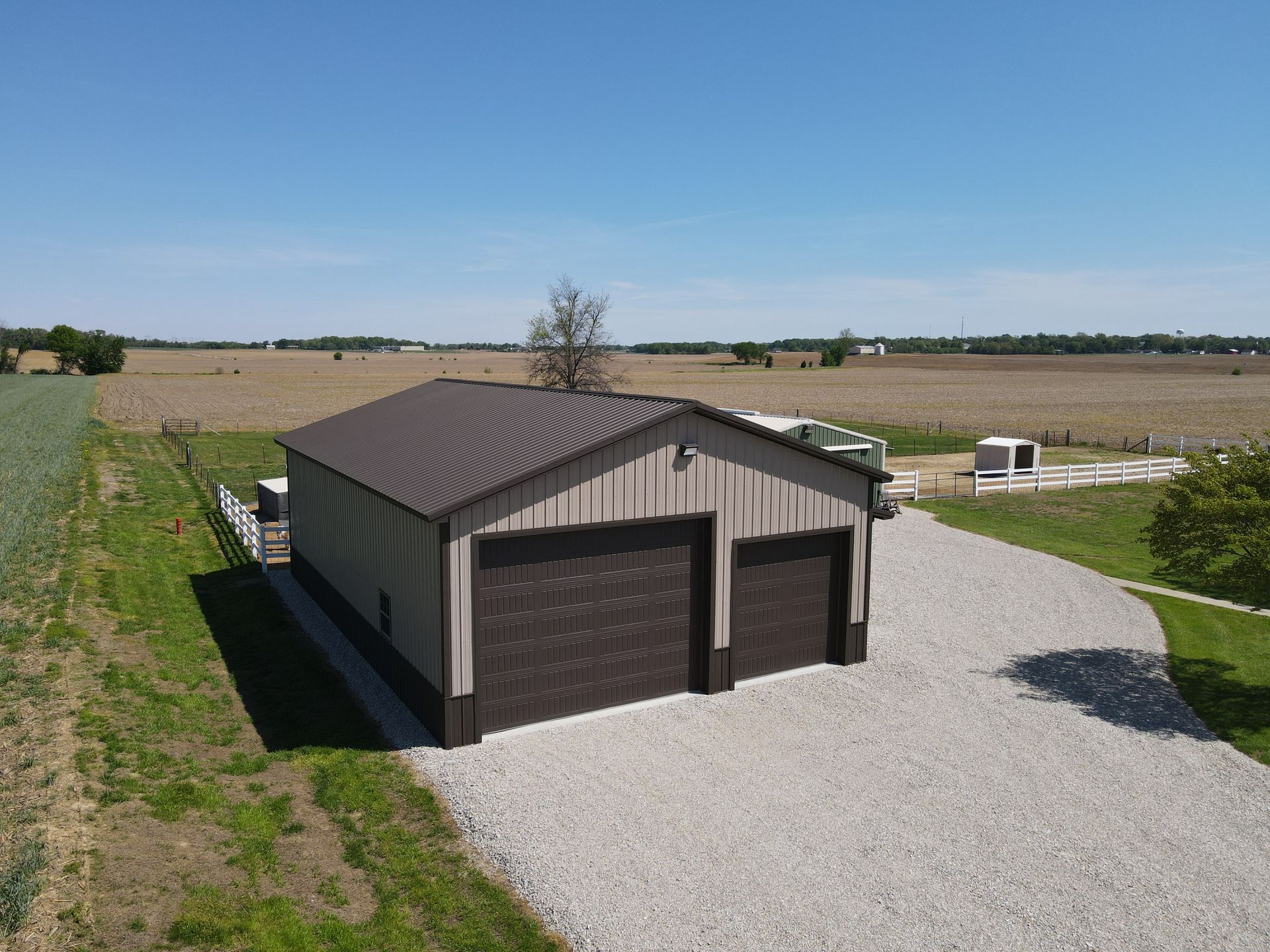 Small brown metal garage on gravel driveway in open rural field under blue sky