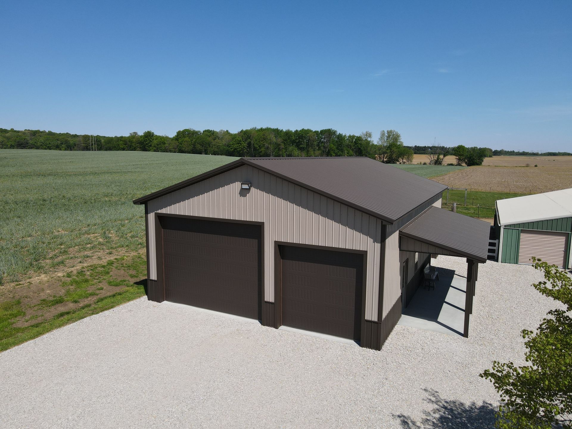 Detached gray garage with two dark doors on a gravel drive in a rural field setting