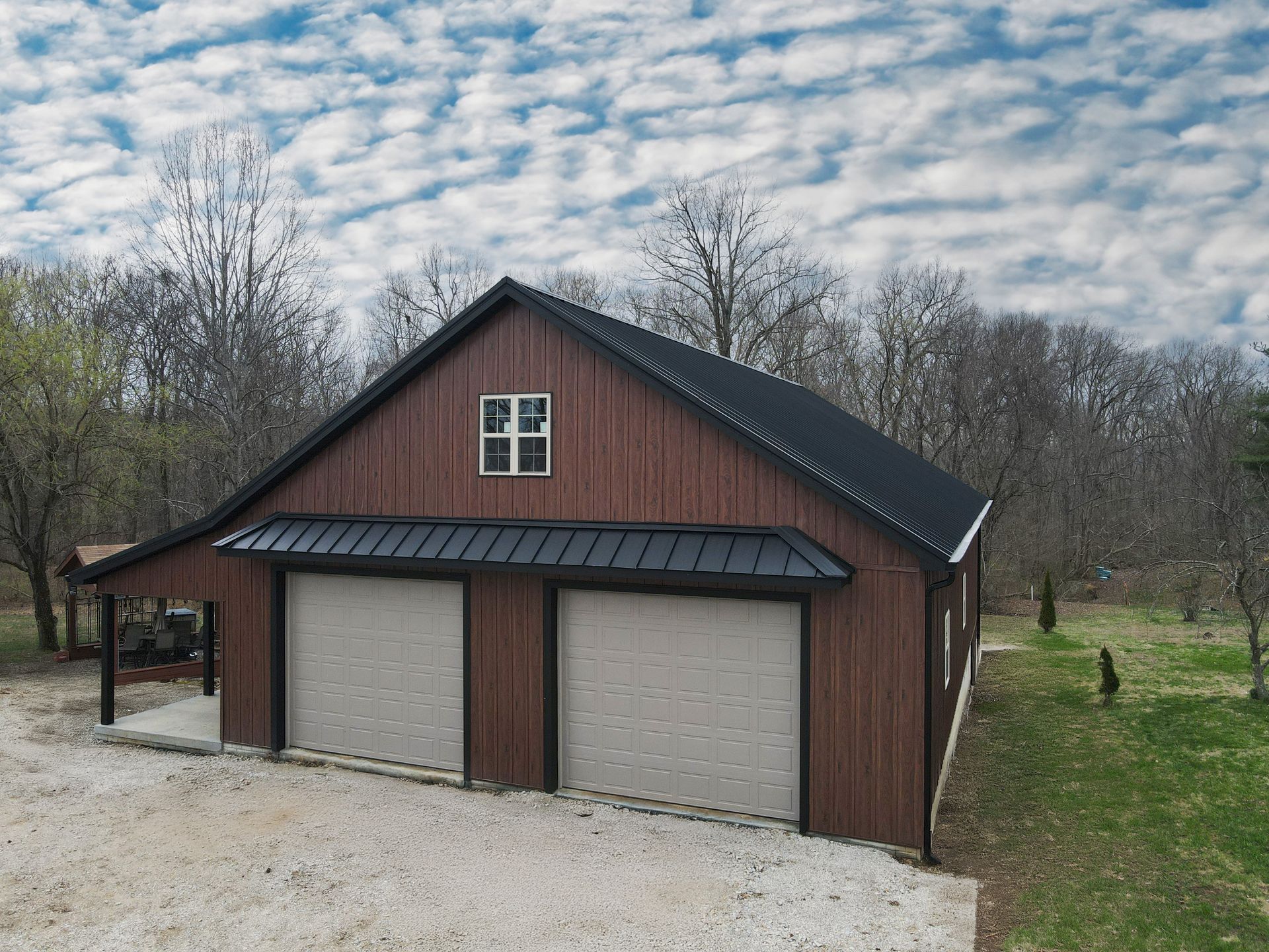 Two-car detached garage with brown siding and beige doors in a rural yard under a cloudy sky