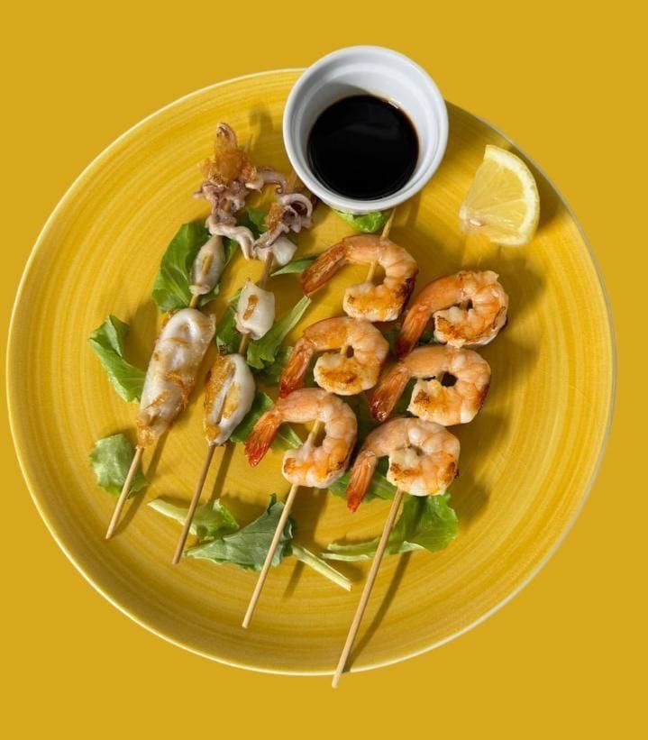 Un piatto giallo condito con gamberi, calamari e salsa