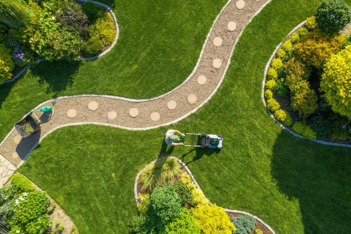 Overhead view of a person mowing a manicured lawn with a winding stone path and surrounding greenery.