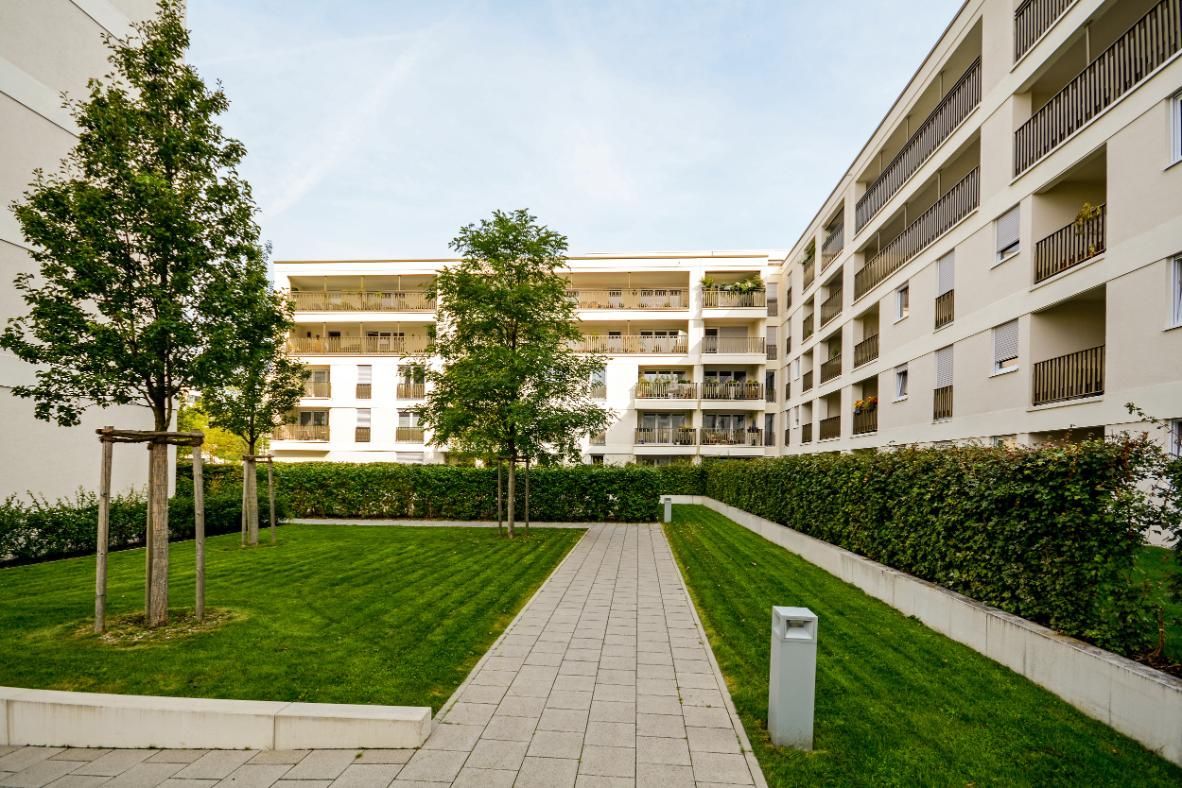 Courtyard of apartment complex with grass, trees, and walkway leading to buildings.