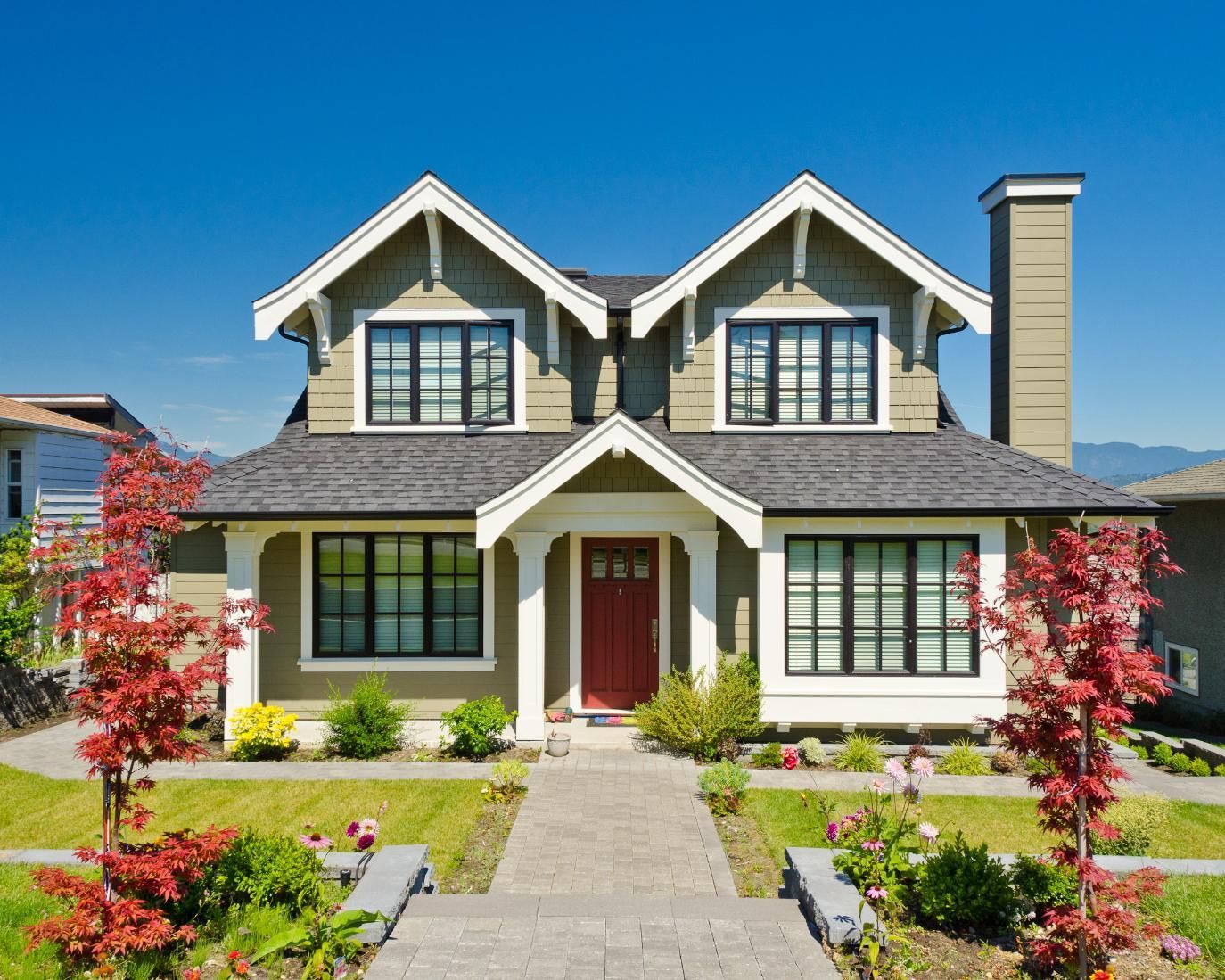 Green house with black window frames, red door, and grey roof. Stone walkway leads to the entrance.