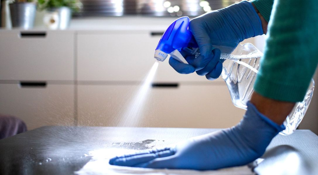 A person wearing blue gloves is cleaning a table with a spray bottle.