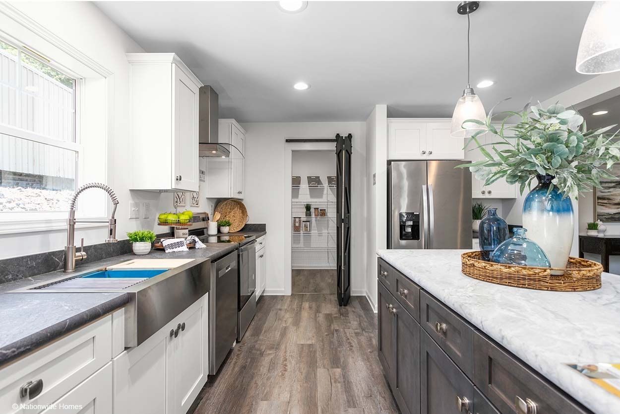 A modern living room with a black fireplace wall, light wood floors, a beige sectional sofa, and a kitchen in the background.
