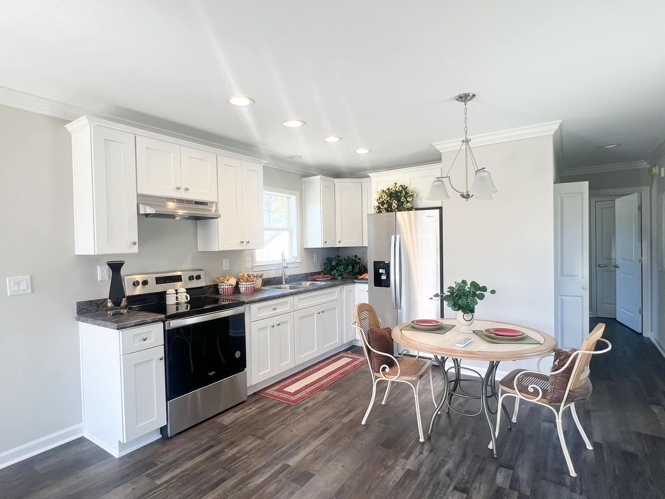 A bright kitchen with white cabinets, stainless steel appliances, dark wood-look floors, and a small round dining table.
