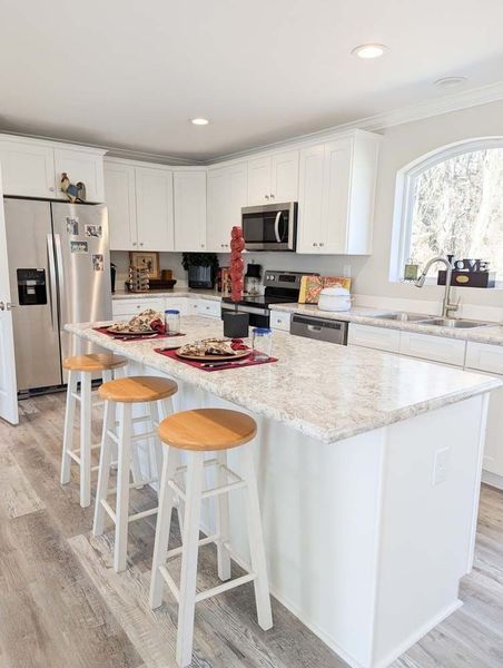 A bright, modern kitchen featuring white cabinets, stainless steel appliances, a marble-topped island, and bar stools.