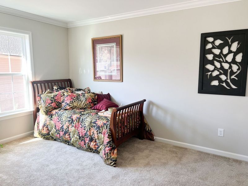 A bedroom with a wooden bed featuring floral bedding, a window, a framed picture, and a black wall art piece.