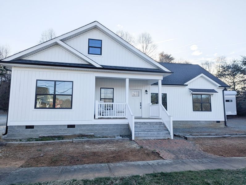 A one-story modern farmhouse with white vertical siding, a covered front porch, and a dark shingled roof.