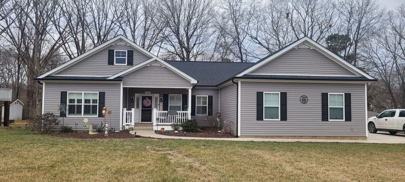 A single-story gray house with black shutters, a covered front porch, and a white truck parked in the side driveway.