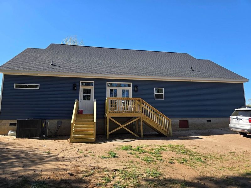 A dark blue residential house exterior with a wooden deck and staircase, under a bright blue sky.
