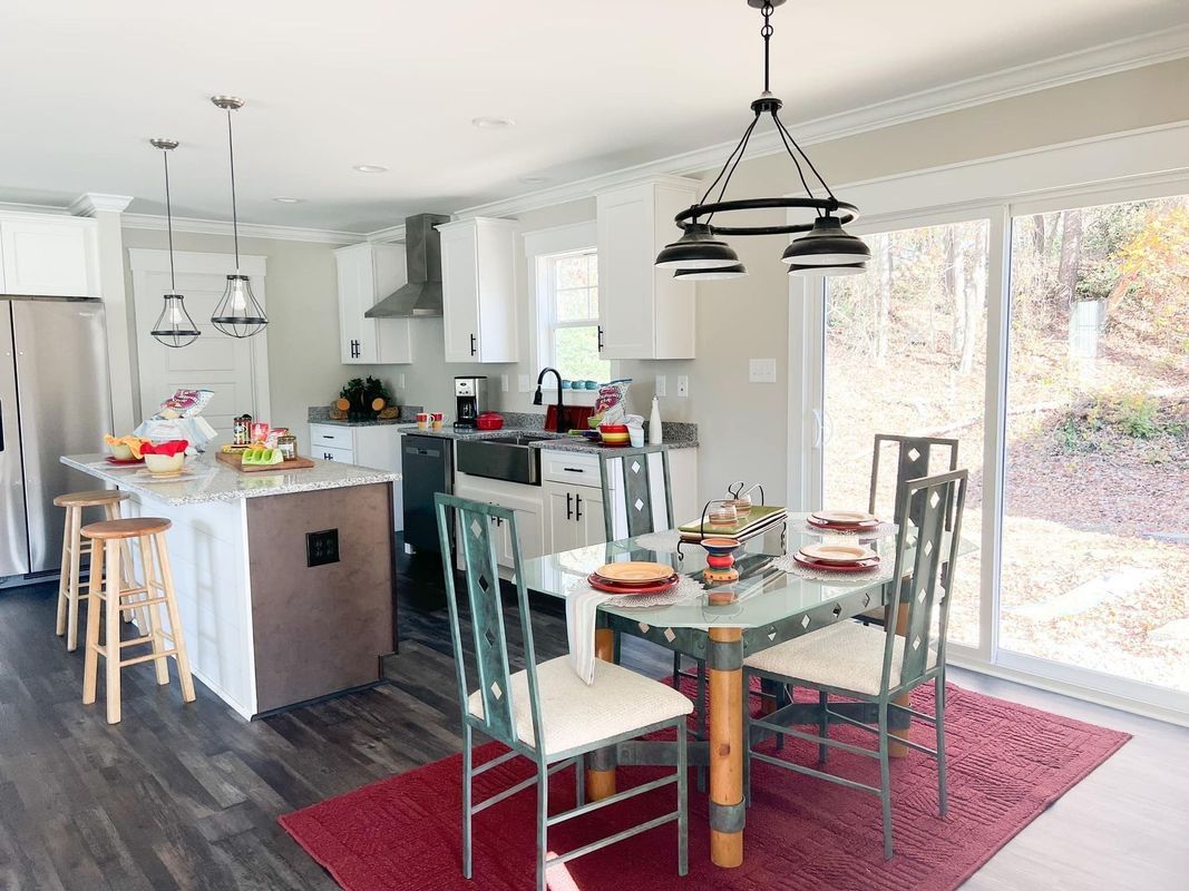 A modern kitchen and dining area with white cabinets, a kitchen island with bar stools, and a dining set on a red rug.